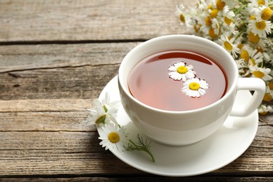 Photo of Aromatic tea in cup and chamomile flowers on wooden table, closeup