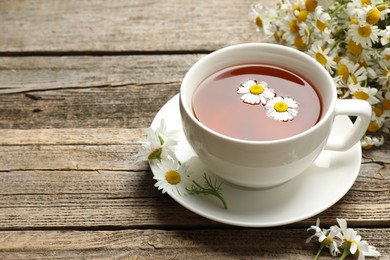 Photo of Aromatic tea in cup and chamomile flowers on wooden table, closeup