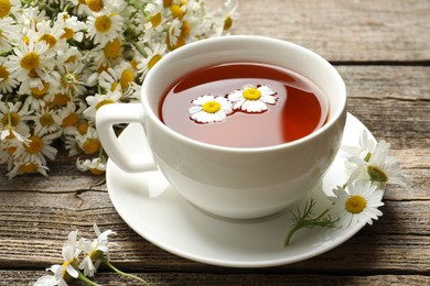 Photo of Aromatic tea in cup and chamomile flowers on wooden table, closeup