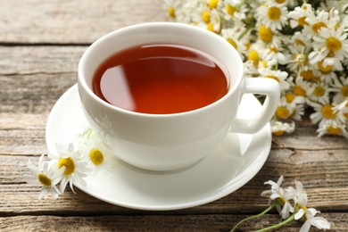 Photo of Aromatic tea in cup and chamomile flowers on wooden table, closeup