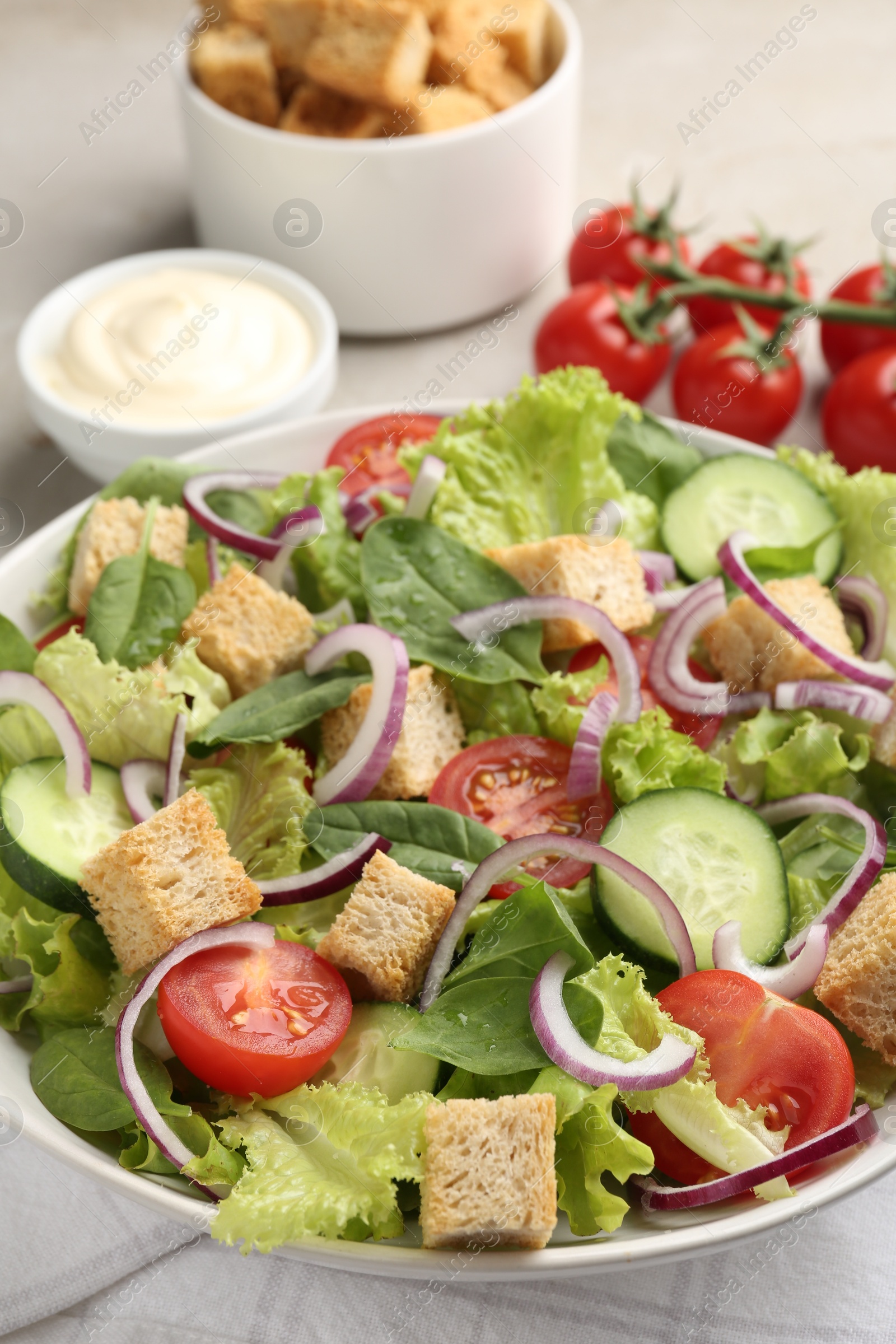 Photo of Delicious salad with croutons and vegetables served on light grey table, closeup