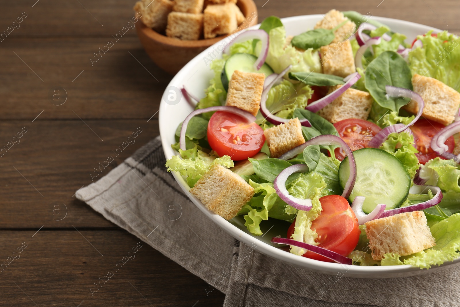 Photo of Delicious salad with croutons and vegetables on wooden table, closeup. Space for text