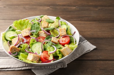 Photo of Delicious salad with croutons and vegetables on wooden table, closeup. Space for text