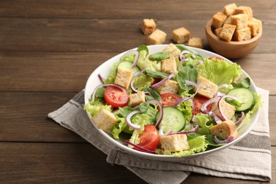 Photo of Delicious salad with croutons and vegetables on wooden table, closeup. Space for text