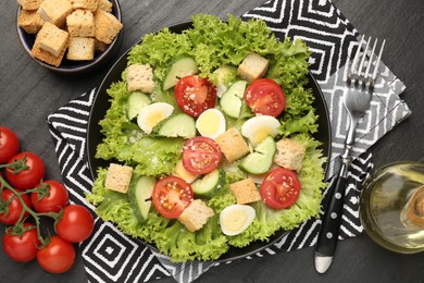 Photo of Delicious salad with croutons and ingredients on black table, flat lay