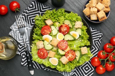 Photo of Delicious salad with croutons and ingredients on black table, flat lay
