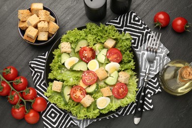 Photo of Delicious salad with croutons and ingredients on black table, flat lay