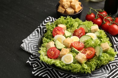 Photo of Delicious salad with croutons and ingredients on black table, closeup. Space for text