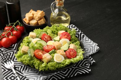 Photo of Delicious salad with croutons and ingredients on black table, closeup. Space for text