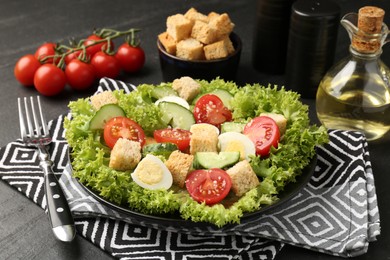 Photo of Delicious salad with croutons and ingredients on black table, closeup