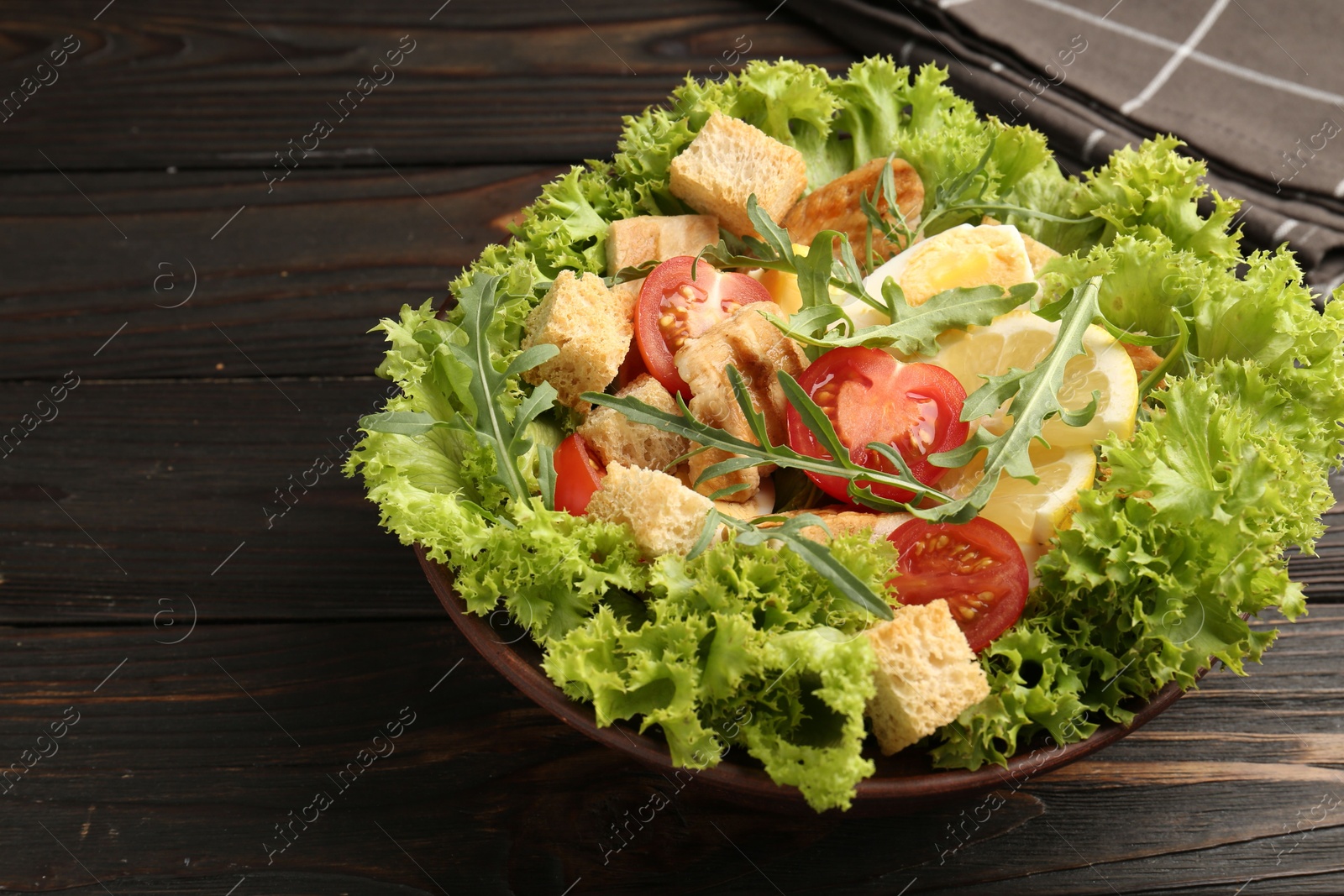 Photo of Delicious salad with croutons, chicken, egg, vegetables, lemon and arugula on wooden table, closeup. Space for text