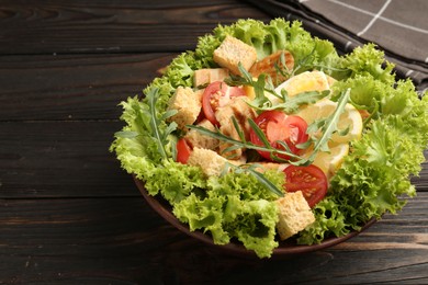 Photo of Delicious salad with croutons, chicken, egg, vegetables, lemon and arugula on wooden table, closeup. Space for text