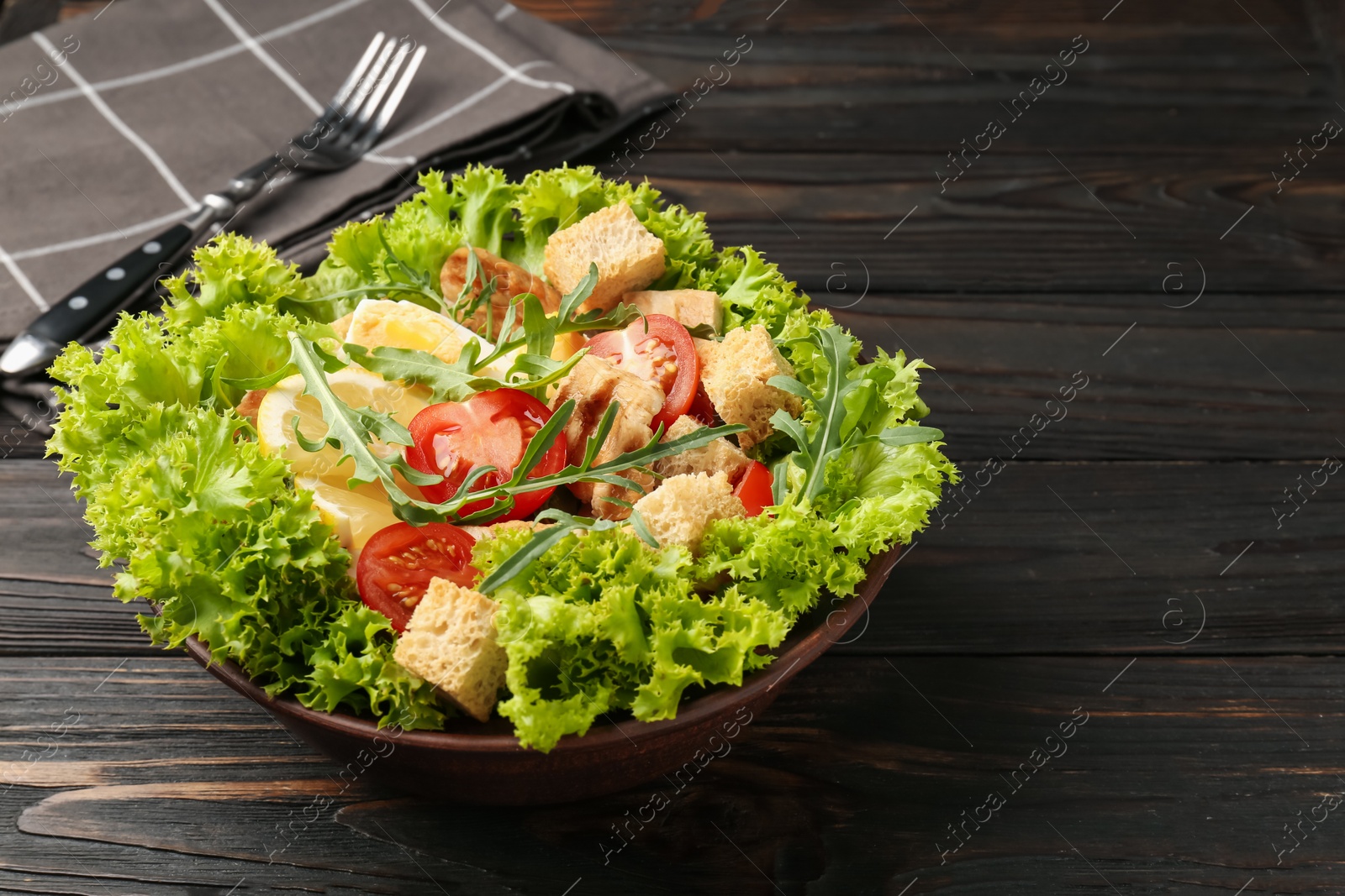Photo of Delicious salad with croutons, chicken, egg, vegetables, lemon and arugula on wooden table, closeup. Space for text