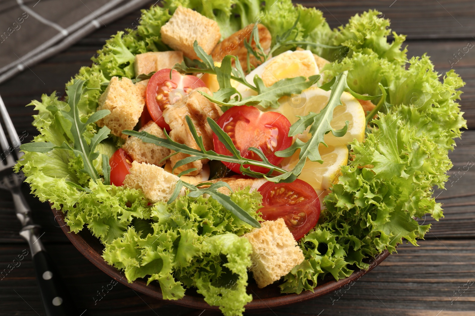 Photo of Delicious salad with croutons, chicken, egg, vegetables, lemon and arugula on wooden table, closeup
