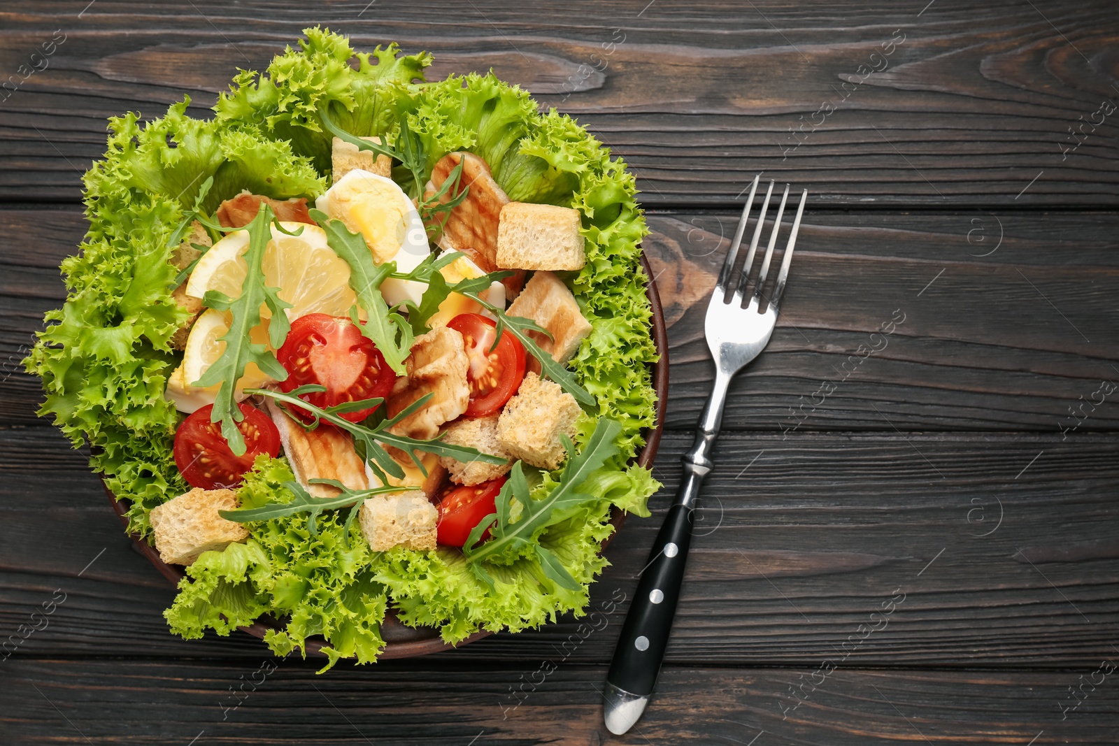 Photo of Delicious salad with croutons, chicken, egg, vegetables, lemon and arugula on wooden table, flat lay. Space for text