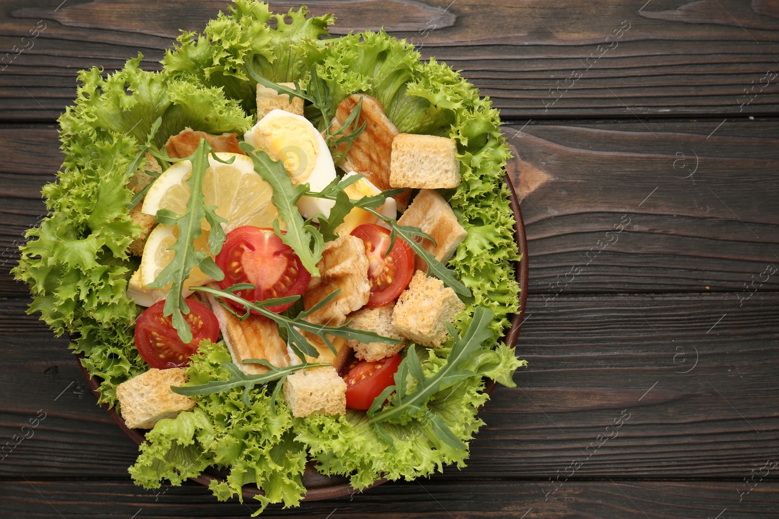 Photo of Delicious salad with croutons, chicken, egg, vegetables, lemon and arugula on wooden table, top view. Space for text