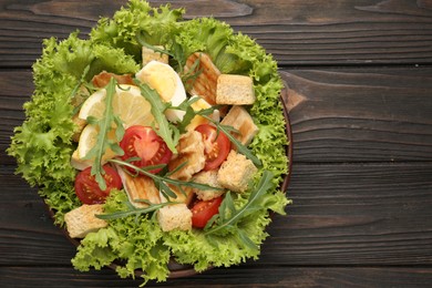 Photo of Delicious salad with croutons, chicken, egg, vegetables, lemon and arugula on wooden table, top view. Space for text