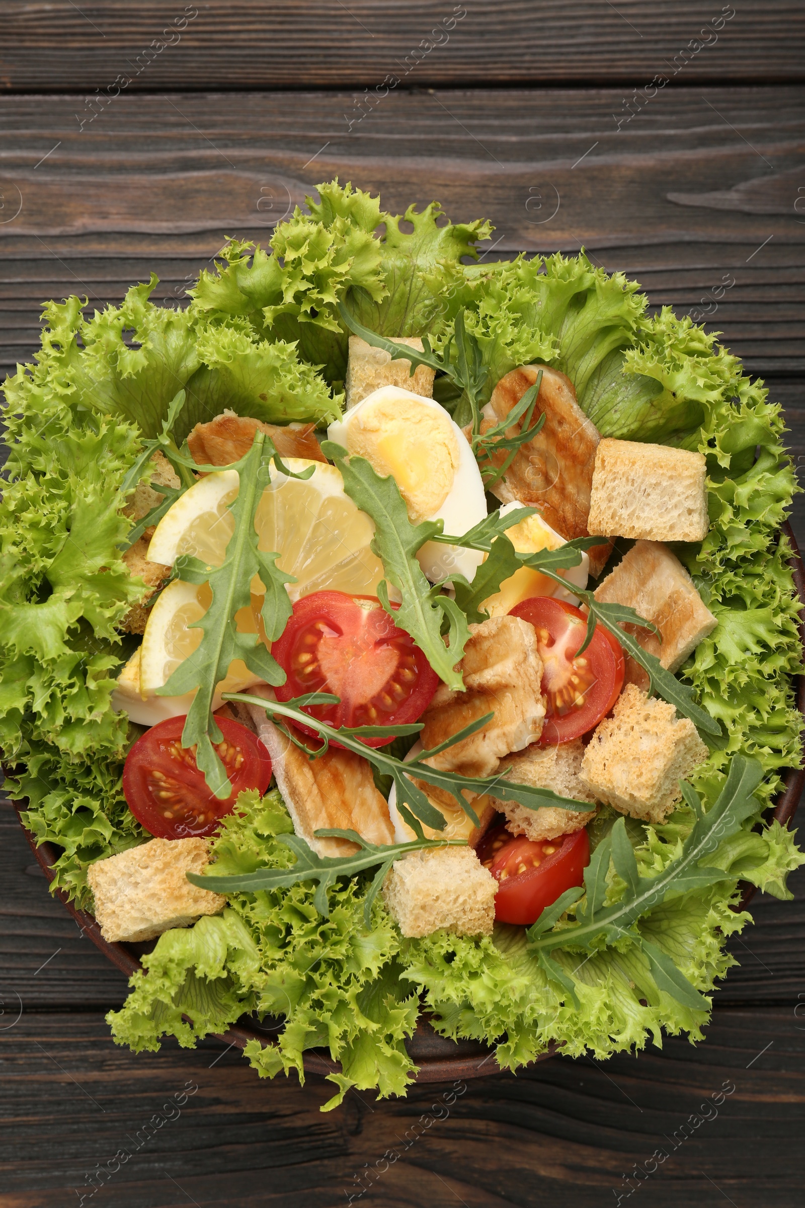 Photo of Delicious salad with croutons, chicken, egg, vegetables, lemon and arugula on wooden table, top view