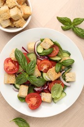 Photo of Delicious salad with croutons, vegetables and basil on wooden table, flat lay