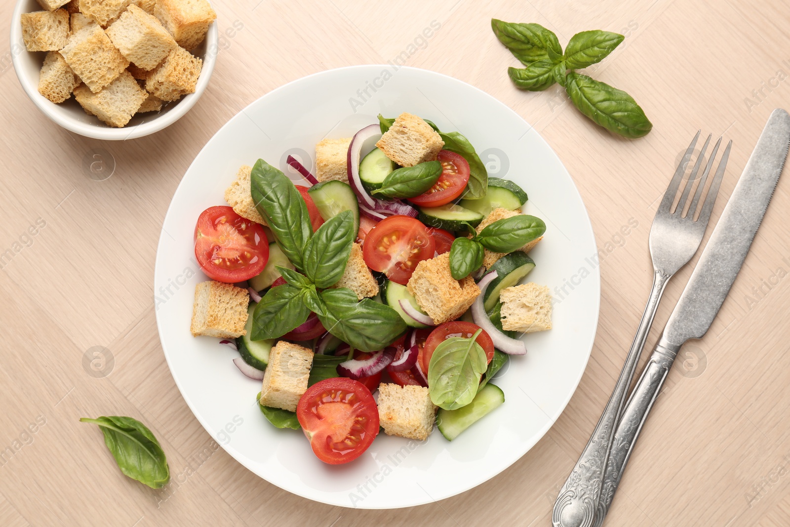 Photo of Delicious salad with croutons, vegetables and basil on wooden table, flat lay