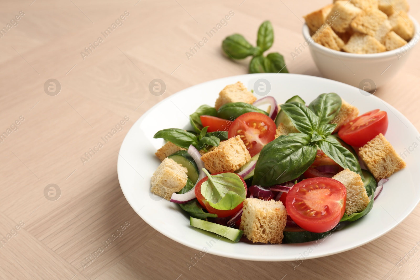 Photo of Delicious salad with croutons, vegetables and basil on wooden table, closeup. Space for text