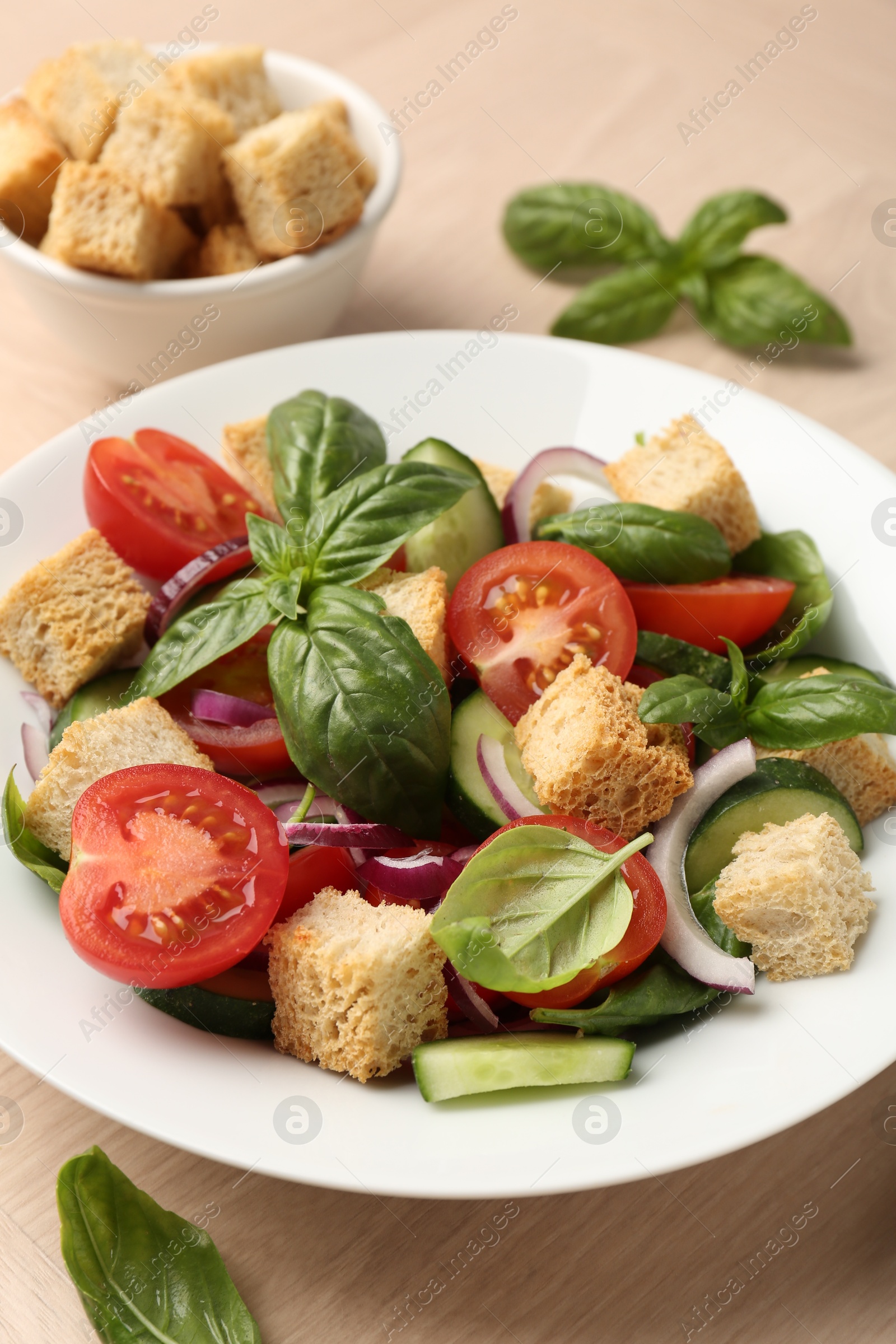 Photo of Delicious salad with croutons, vegetables and basil on wooden table, closeup