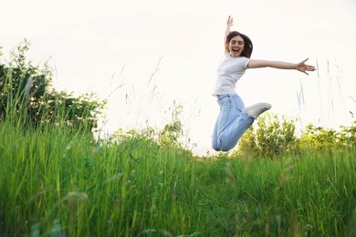 Photo of Feeling freedom. Happy young woman jumping in nature, space for text