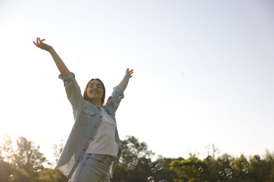 Photo of Feeling freedom. Happy young woman enjoying time in nature among soap bubbles, low angle view. Space for text