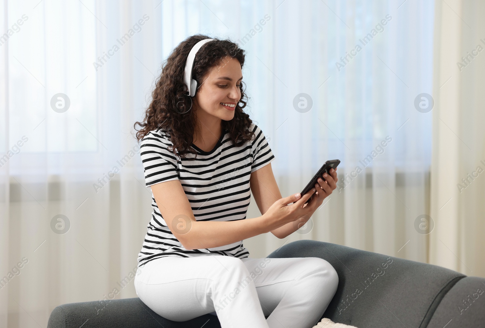 Photo of Young woman with headphones and smartphone listening to music at home