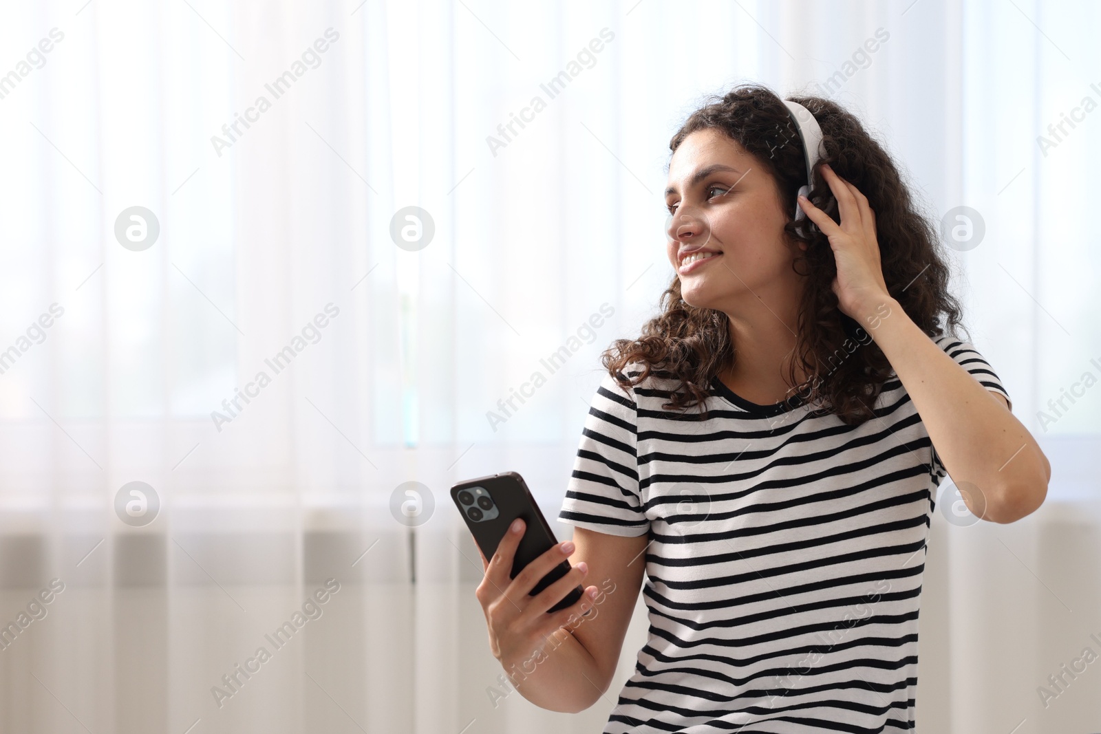 Photo of Young woman with headphones and smartphone listening to music at home, space for text
