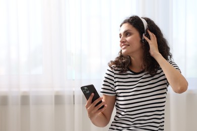 Photo of Young woman with headphones and smartphone listening to music at home, space for text