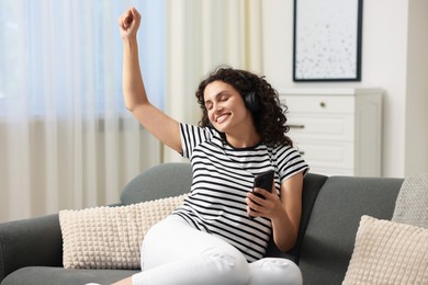 Photo of Young woman with headphones and smartphone listening to music at home