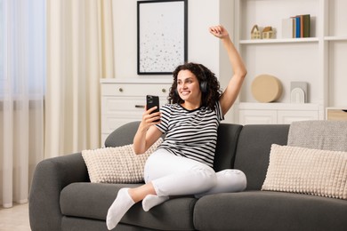 Photo of Young woman with headphones and smartphone listening to music at home