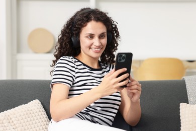 Photo of Young woman with headphones and smartphone listening to music at home