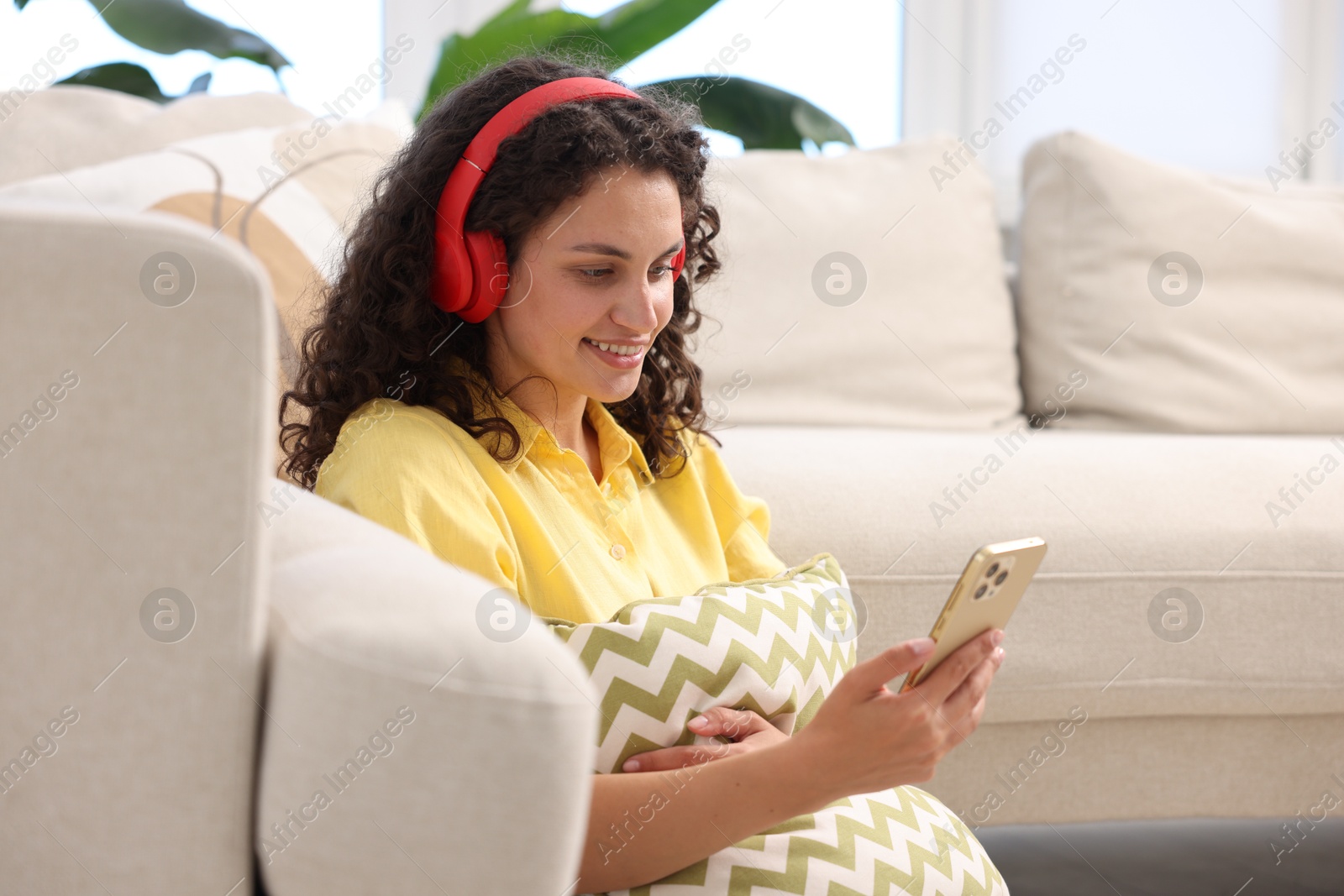 Photo of Young woman with headphones and smartphone listening to music at home