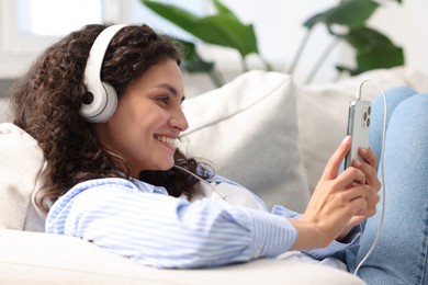 Photo of Young woman with headphones and smartphone listening to music at home