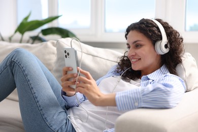 Photo of Young woman with headphones and smartphone listening to music at home