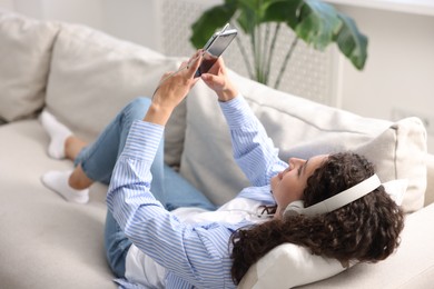 Photo of Young woman with headphones and smartphone listening to music at home