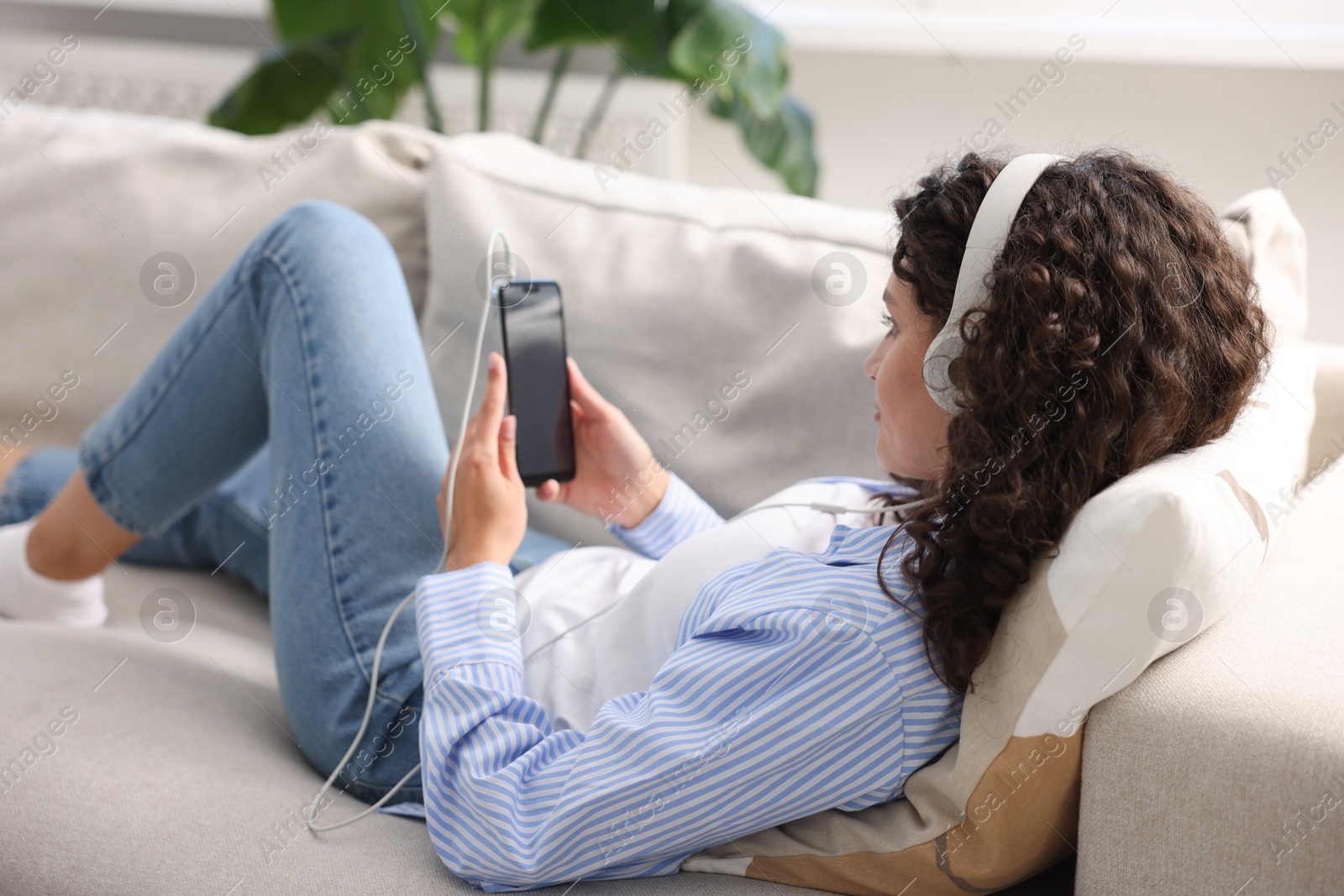 Photo of Young woman with headphones and smartphone listening to music at home