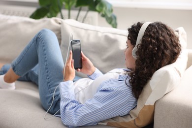 Photo of Young woman with headphones and smartphone listening to music at home