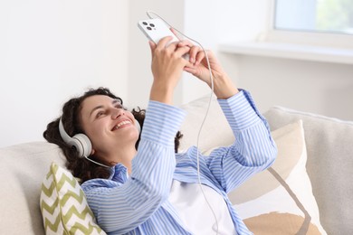 Photo of Young woman with headphones and smartphone listening to music at home