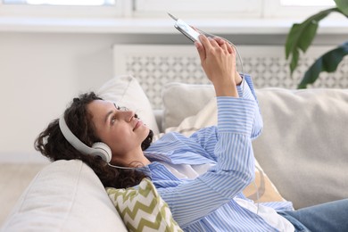 Photo of Young woman with headphones and smartphone listening to music at home