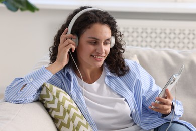 Photo of Young woman with headphones and smartphone listening to music at home
