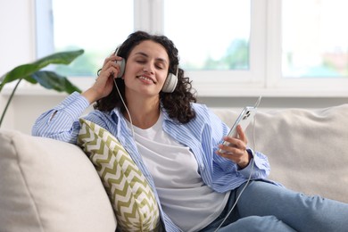 Photo of Young woman with headphones and smartphone listening to music at home