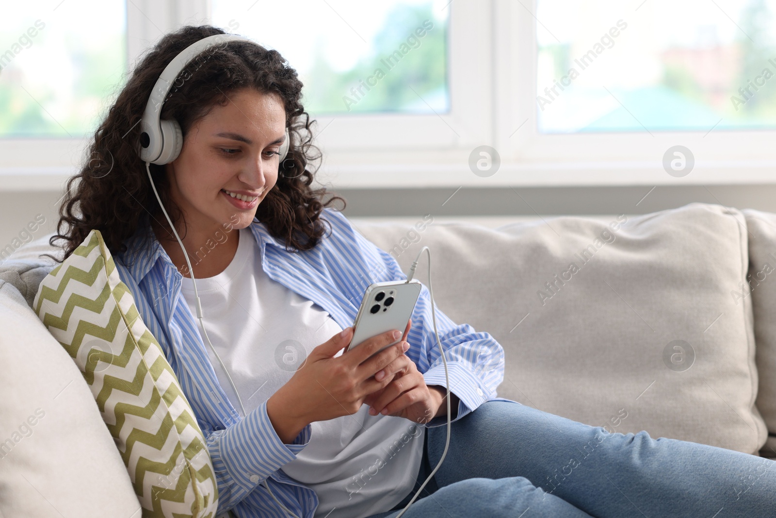 Photo of Young woman with headphones and smartphone listening to music at home