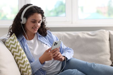 Photo of Young woman with headphones and smartphone listening to music at home