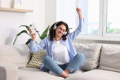 Photo of Young woman with headphones and smartphone listening to music at home