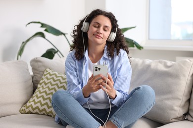 Photo of Young woman with headphones and smartphone listening to music at home