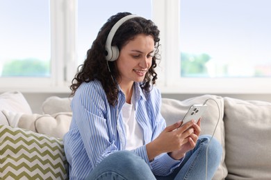 Photo of Young woman with headphones and smartphone listening to music at home