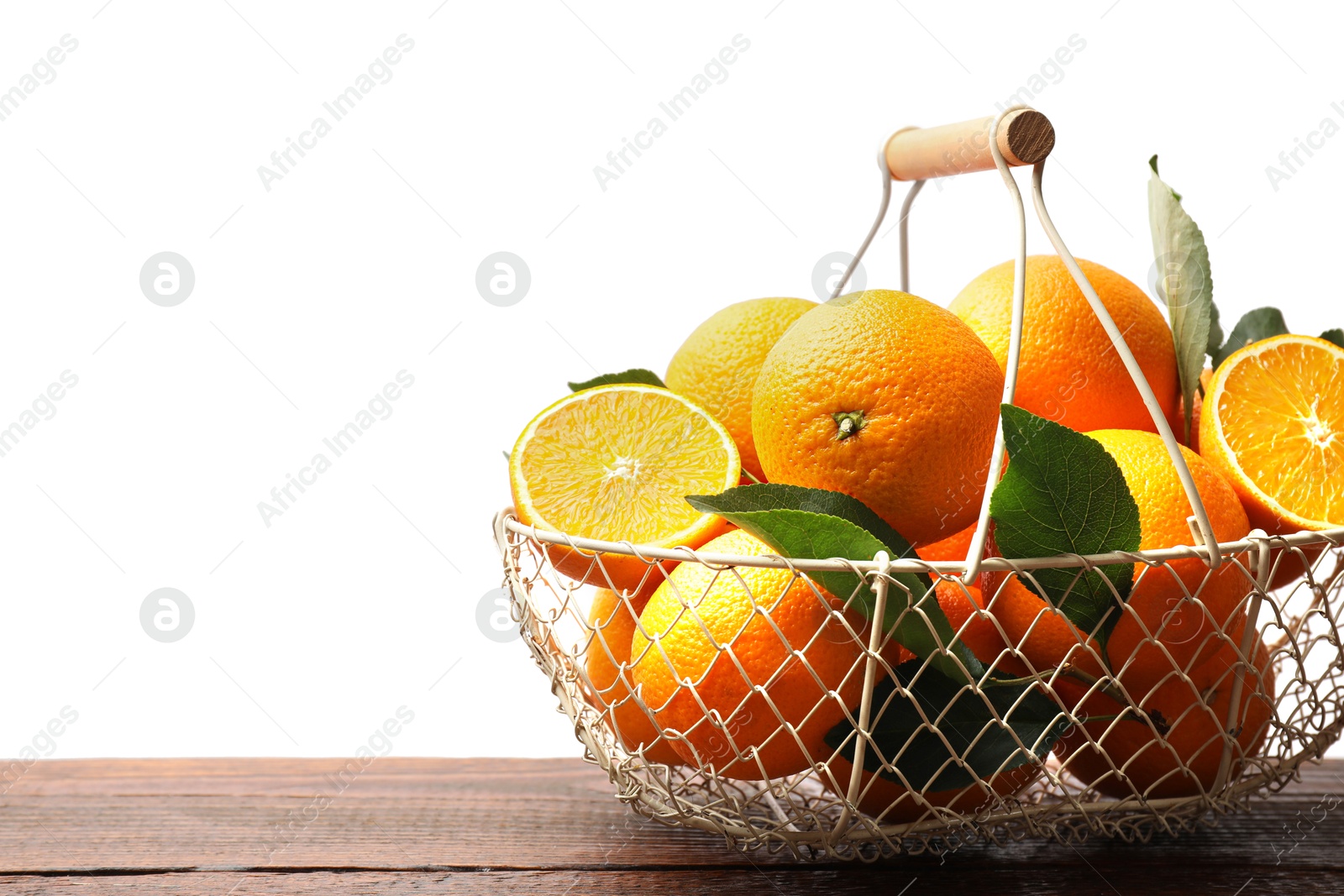 Photo of Juicy oranges and green leaves in metal basket on wooden table against white background. Space for text